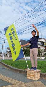 のぼりの横に立って手を挙げる平山ゆうやの写真